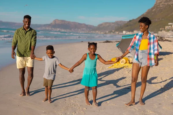 幸せなアフリカ系アメリカ人の若い両親と子供たちは 空に向かってビーチに立って手を握っています 変わらないビーチ 子供時代 ライフスタイル 楽しみそして休日 — ストック写真