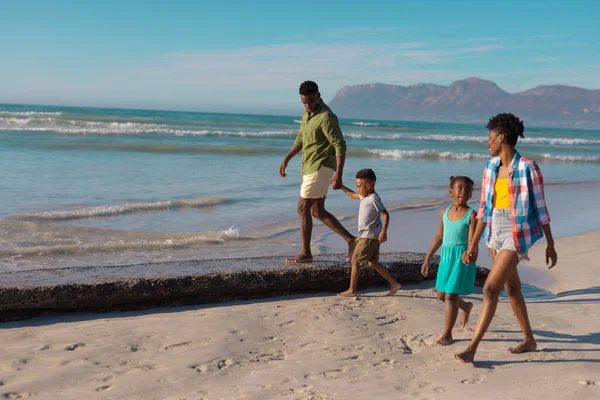 アフリカ系アメリカ人の若い両親は 娘と息子の手を持ちながらビーチで空に向かって歩いています 変わらない ビーチ 子供時代 ライフスタイル 楽しみと休日 — ストック写真