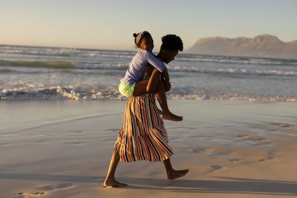 澄んだ空に向かってビーチを歩いている間 遊び心のあるアフリカ系アメリカ人の若い女性のピギーバックの娘 コピースペース 変わらない 子供時代 一緒に ライフスタイル 楽しみ — ストック写真