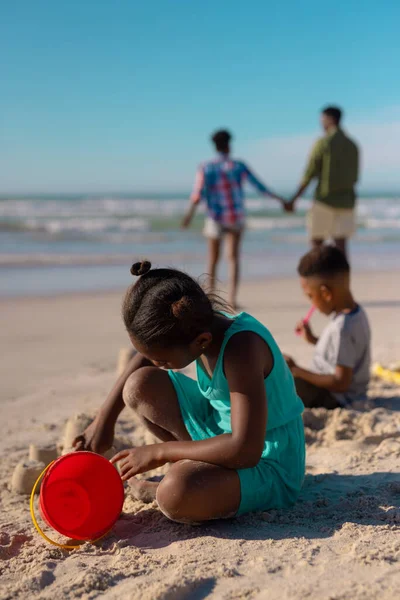 非洲裔美国女孩 带着桶在海滩上做沙堡 背对着天空 有家人背景 复制空间 生活方式 — 图库照片