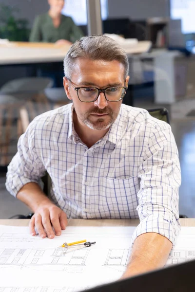 自信的高加索男性工程师坐在工作场所的办公桌前 一边使用笔记本电脑 一边手握蓝图 不变的 创造性的商业 技术和现代办公概念 — 图库照片