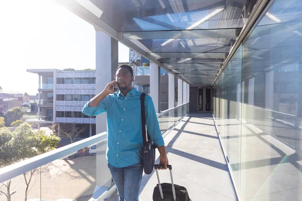 若いアフリカ系アメリカ人ビジネスマンが空港でスマートフォンで話をしながら荷物を持って歩く 変化のない技術職業ビジネス旅行交通の概念 — ストック写真