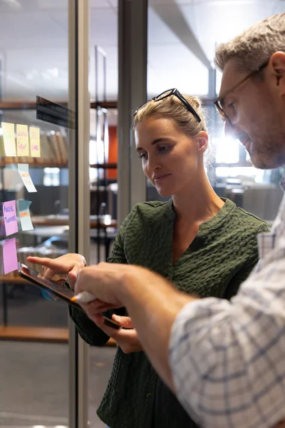 Confident caucasian colleagues discussing together on digital tablet while planning at workplace. unaltered, creative business, technology, teamwork and modern office concept.