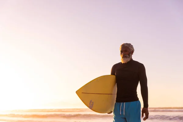 アフリカ系アメリカ人のひげを生やした老人は 日没時に海と澄んだ空に向かってサーフボードを持っている コピースペース 変更なし 水生スポーツ 休日とアクティブなライフスタイルの概念 — ストック写真