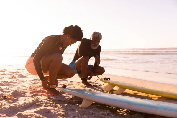 アフリカ系アメリカ人のカップルは日没時に澄んだ空に対してビーチで足首にサーフボードの文字列を結ぶ コピースペース 変わらない 水生スポーツ アクティブなライフスタイルの概念 — ストック写真
