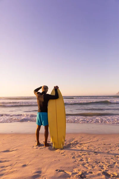 サーフボードを持つアフリカ系アメリカ人のシニア男性の背面ビューは 澄んだ空に対して海を見て コピースペース 変更なし 水上スポーツ アクティブなライフスタイルのコンセプト — ストック写真