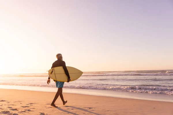 Afrykański Starszy Pan Deską Surfingową Spacerujący Plaży Przed Bezchmurnym Niebem — Zdjęcie stockowe
