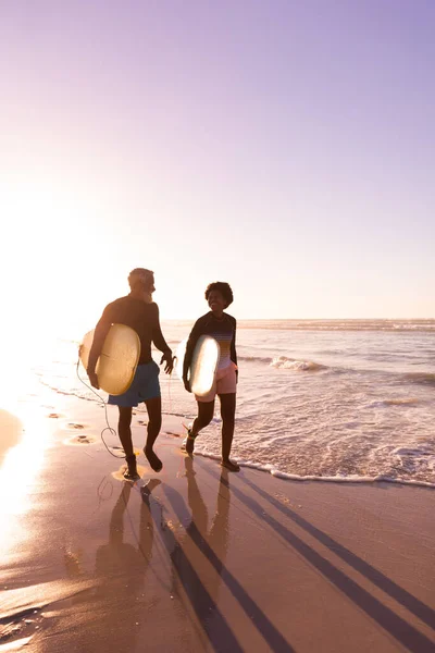 快乐的非洲裔美国夫妇 在日落时分 与冲浪板在岸上迎着晴朗的天空散步 复制空间 水上运动 积极的生活方式 — 图库照片