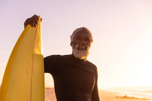 アフリカ系アメリカ人の髭を生やした老人を笑顔にし サーフボードをはっきりとした空に向かってビーチに立っている コピースペース 変更なし 水上スポーツ 休日とアクティブなライフスタイルの概念 — ストック写真