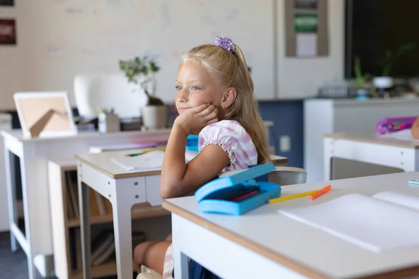 Kaukázusi Általános Iskolás Lány Kezével Állán Félrenéz Miközben Osztályteremben Asztalnál — Stock Fotó