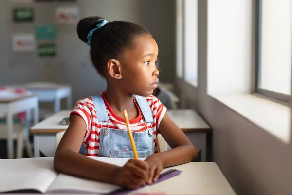 Bedachtzaam Afrikaans Amerikaans Basisschoolmeisje Dat Wegkijkt Terwijl Aan Een Bureau — Stockfoto