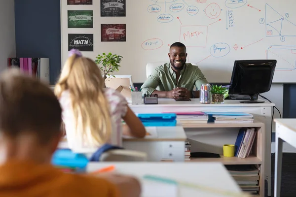 アフリカ系アメリカ人の若い男性教師の肖像教室で勉強している学生と机の上に座っている 変化のない教育学習子供時代教育職業学校の概念 — ストック写真