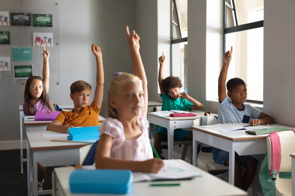 Multirassische Grundschüler Heben Die Hände Während Sie Schreibtisch Klassenzimmer Sitzen — Stockfoto