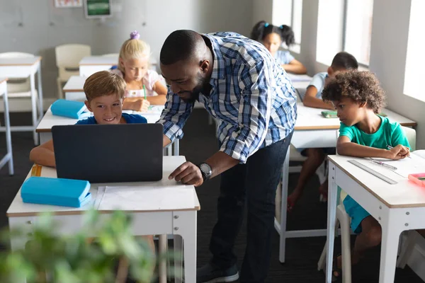 非洲裔美国男教师在课桌前向高加索小学生展示笔记本电脑 无线技术和学校概念 — 图库照片