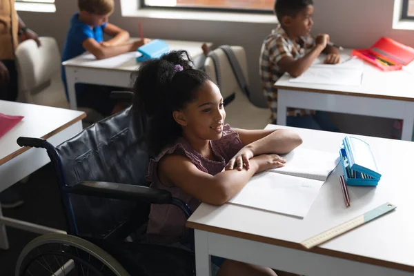 坐在轮椅上的小学女生微笑着坐在课桌前 身体残疾和学校观念 — 图库照片