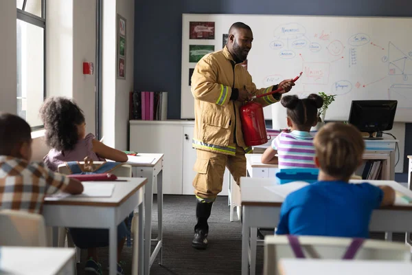African american young male teacher in uniform teaching fire extinguisher to multiracial students. unaltered, education, firefighter, safety, protection, teaching and school concept.
