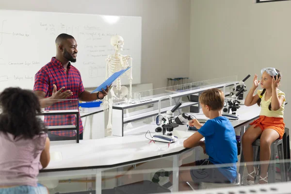 アフリカ系アメリカ人の若い男性教師が実験室で多人種の小学生に教える 変化のない教育子供時代学習科学システム教育学校の概念 — ストック写真