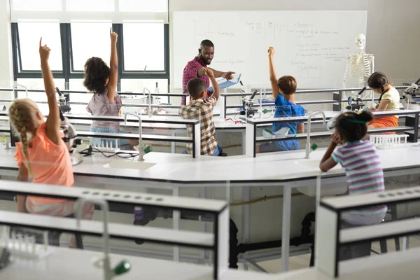 アフリカ系アメリカ人の若い男性教師が質問している間に手を挙げている多人種の小学生 変更されず教育 システム 学校の概念 — ストック写真