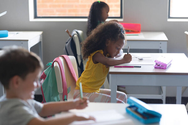 Multiracial Elementary School Students Writing Book While Studying Desk Classroom Stock Photo