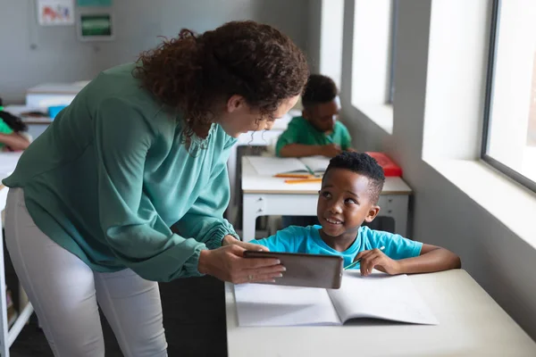 アフリカ系アメリカ人の小学生が若い女性の白人教師をデジタルタブレットで見ています 変化のない教育子供時代職業技術教育学校の概念 — ストック写真
