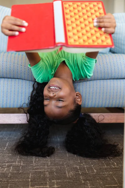 在学校里躺在沙发上 笑着看美国小学女生的书 学习和学校观念 — 图库照片