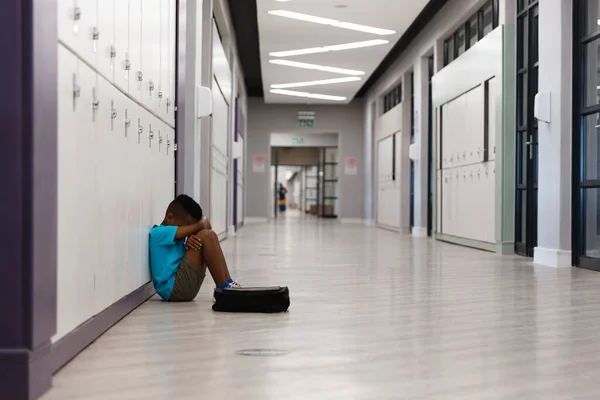 非洲裔美国小学生坐在走廊地板上抱膝的侧视图 孤独和学校观念 — 图库照片