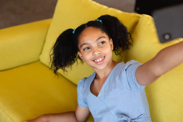 Una Sonriente Colegiala Birracial Tomando Selfie Mientras Está Sentada Sofá — Foto de Stock