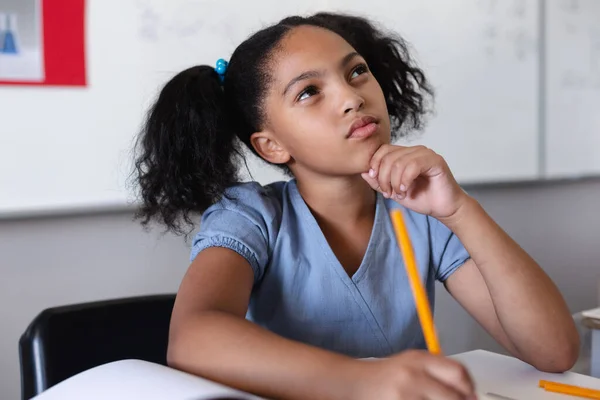 Thoughtful Biracial Elementary Girl Hand Chin Looking While Studying Desk — Stock Photo, Image