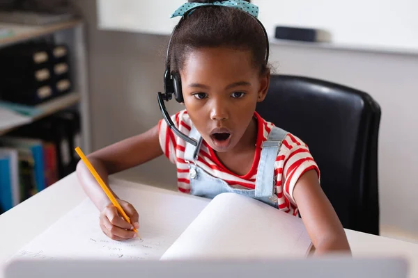 机の上で勉強しながらノートパソコンを開いているアフリカ系アメリカ人の小学生 変更されていない リスニング 無線技術と学校の概念 — ストック写真