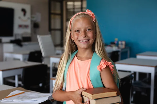 教室に立ちながら本を持っている笑顔の白人小学生の肖像画 変化のない教育子供時代幸せ学校のコンセプト — ストック写真
