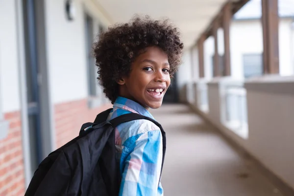 Portret Uśmiechniętego Afrykańskiego Ucznia Podstawówki Oglądającego Się Przez Ramię Szkolnym — Zdjęcie stockowe