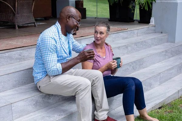 外でコーヒーを飲みながら話す多人種のシニアカップル 変化のないライフスタイル退職共に飲みリフレッシュ — ストック写真