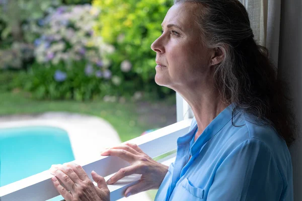 Contemplative Caucasian Senior Woman Looking Away While Standing Window Unaltered — Stock Photo, Image