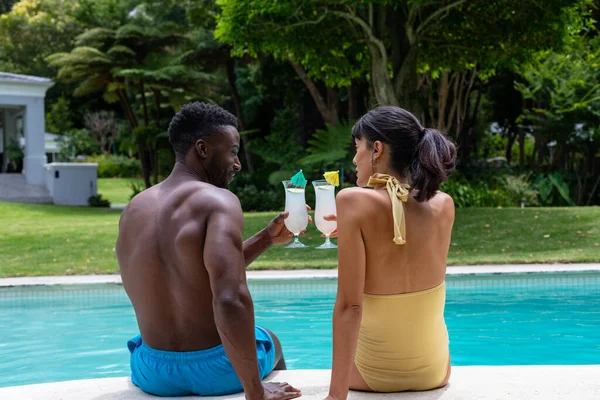 Rear View Multiracial Young Couple Toasting Drinks While Sitting Swimming — Stockfoto