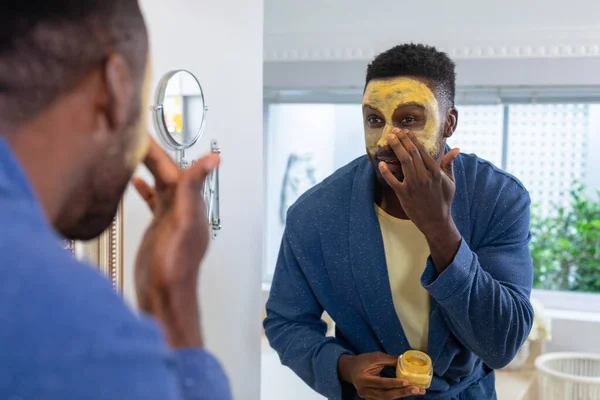 African American Young Man Looking Mirror Applying Facial Mask Bathroom — стоковое фото