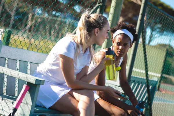 Young Biracial Female Tennis Players Talking While Sitting Bench Court — Foto de Stock