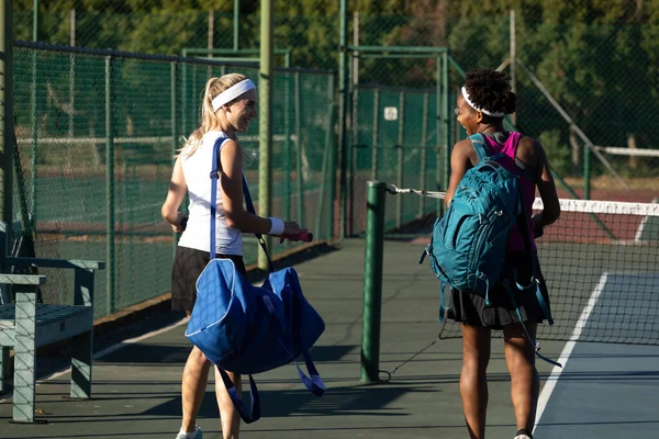 Smiling Multiracial Young Female Tennis Players Walking Bags Court Sunny — Stockfoto