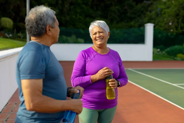 テニスコートで先輩男性と話をする水筒を持った巨乳笑顔の先輩女性 変わらない スポーツ 健康的で活動的なライフスタイルの概念 — ストック写真