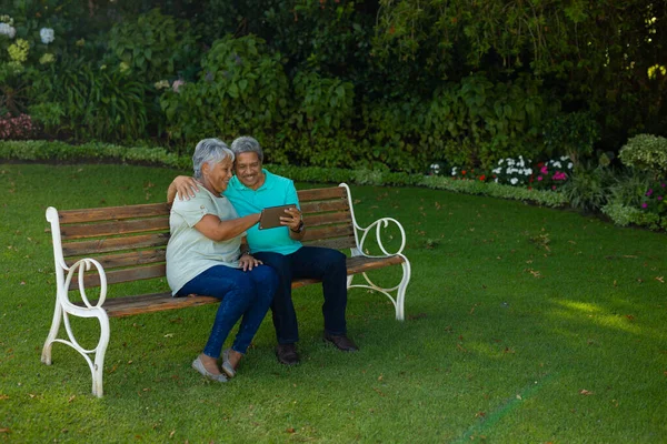 Smiling Biracial Senior Couple Using Digital Tablet While Sitting Bench — ストック写真
