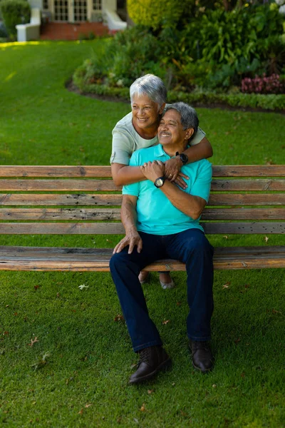 Biracial Smiling Senior Woman Embracing Senior Husband Sitting Bench Looking — Fotografia de Stock