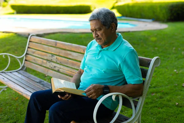 Focused Biracial Senior Man Wearing Blue Shirt Reading Book While — Stock Photo, Image