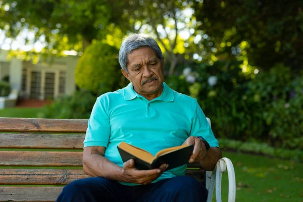 Serious Biracial Senior Man Reading Book Focus While Sitting Bench — Stockfoto