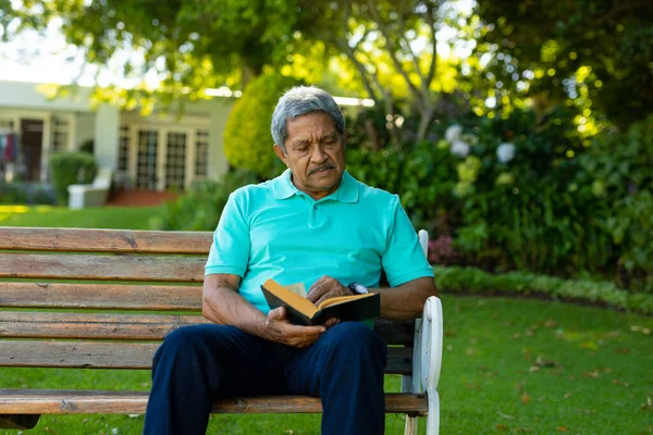 Focused Biracial Senior Man Reading Book While Sitting Bench Trees — Foto de Stock