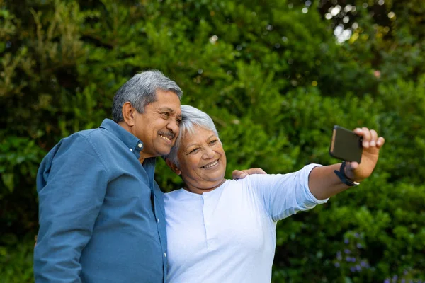 Smiling Biracial Senior Woman Taking Selfie Husband Smart Phone Trees — стоковое фото