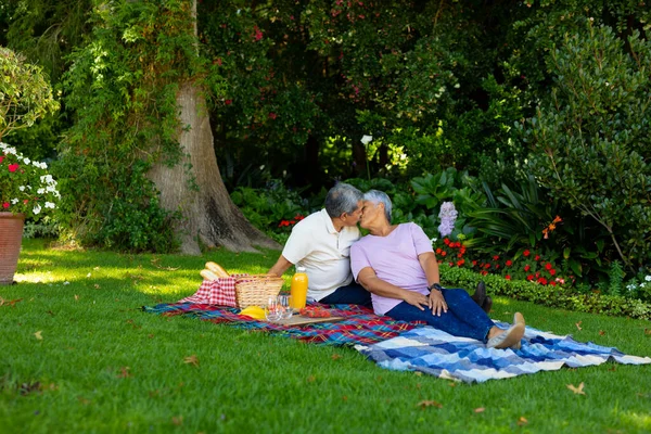 Biracial Senior Couple Kissing While Sitting Food Drink Blanket Plants — Fotografia de Stock