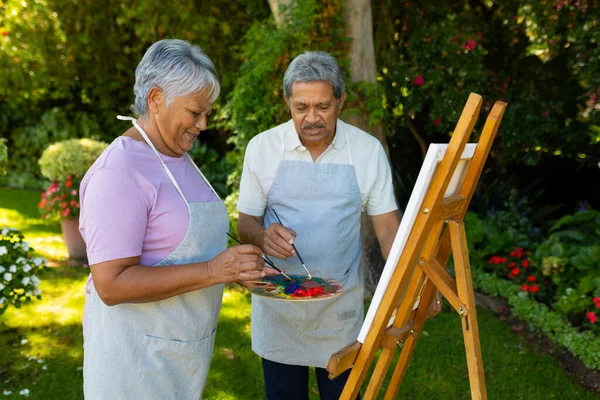 Biracial Senior Couple Wearing Aprons Painting Watercolors Canvas Plants Yard — Stok fotoğraf