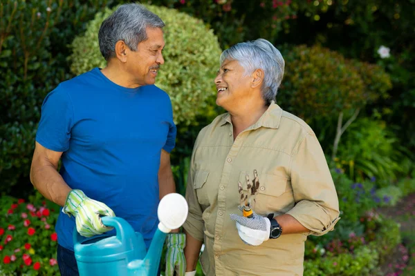Smiling Biracial Senior Couple Holding Watering Can Gardening Fork Looking — Stok fotoğraf