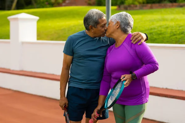 Romantic Biracial Senior Husband Wife Holding Rackets Kissing While Standing — Foto de Stock