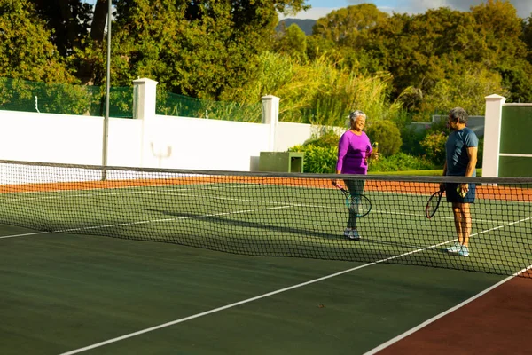 Biracial Senior Couple Talking While Standing Tennis Court Trees Sunny — Stock Fotó