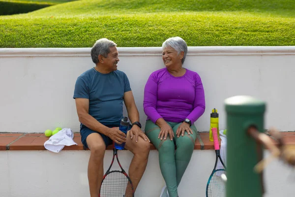 Happy Biracial Senior Couple Talking While Sitting Rackets Water Bottles — Foto de Stock